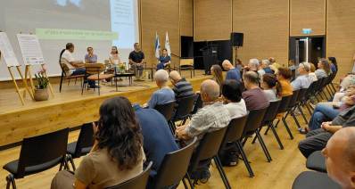 כנס נגד הבנייה בשטחי תע"ש רמת השרון. באולם יושב הקהל מול במה ועליה שישה אנשים.