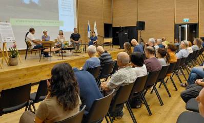 כנס נגד הבנייה בשטחי תע"ש רמת השרון. באולם יושב הקהל מול במה ועליה שישה אנשים.