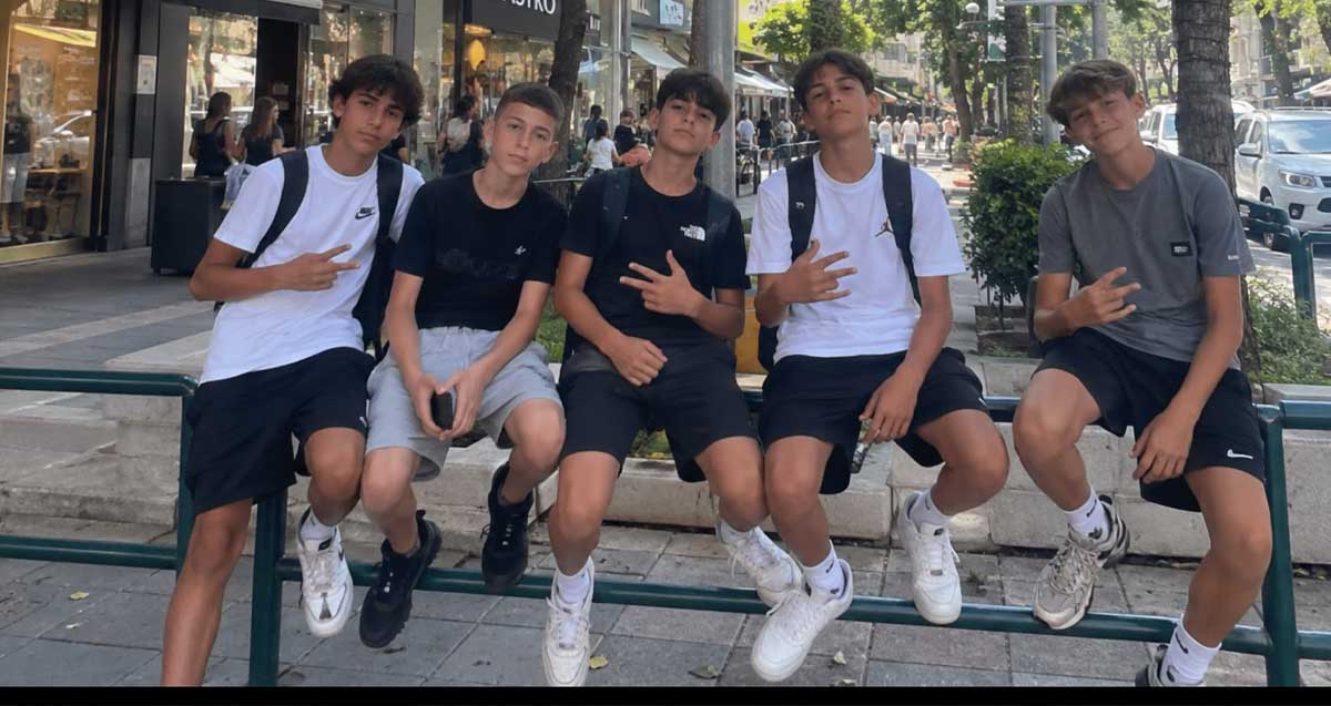 חבורת נערים. איור AI. חמישה צעירים יושבים על הברזלים במדרכה.