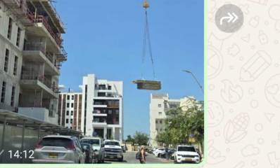 עגורן עם משא כבד מעל רחוב עם הולכי רגל ומכוניות ברעננה