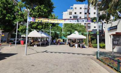 הרצל פינת ויצמן מול בית הכנסת המרכזי. ברחבה מתקיים יריד סוכות ארבעת המינים, תחת שמשיות לבנות.