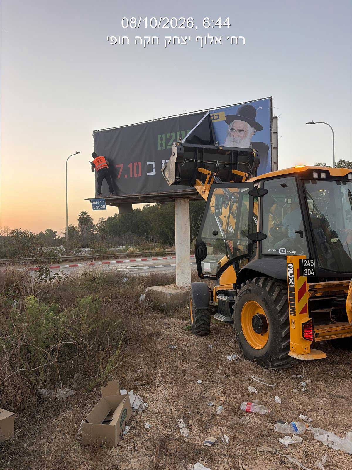 שלט חוצות שהוסר. ליד השלט כלי הנדסי עם כף קדמית. אדם עומד על מדף השלט.