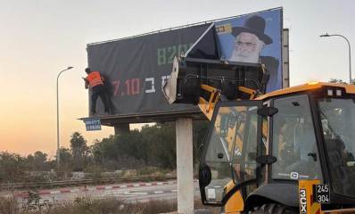 שלט חוצות שהוסר. ליד השלט כלי הנדסי עם כף קדמית. אדם עומד על מדף השלט.