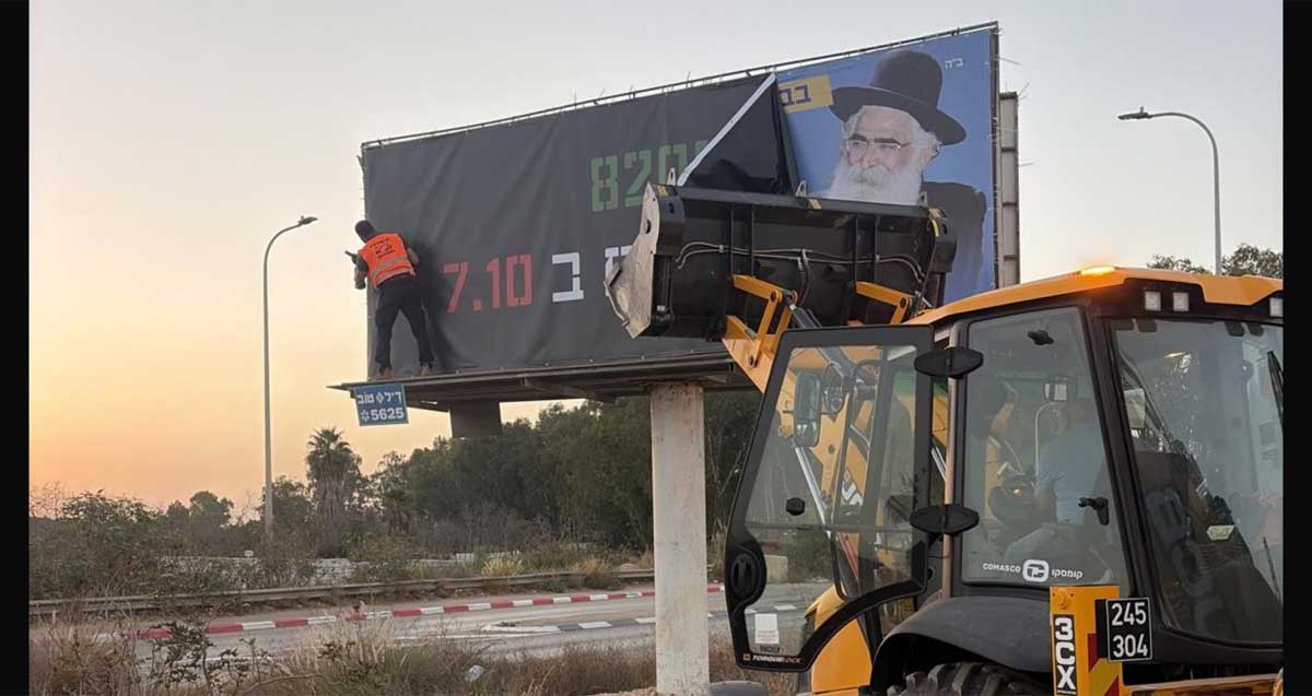 שלט חוצות שהוסר. ליד השלט כלי הנדסי עם כף קדמית. אדם עומד על מדף השלט.